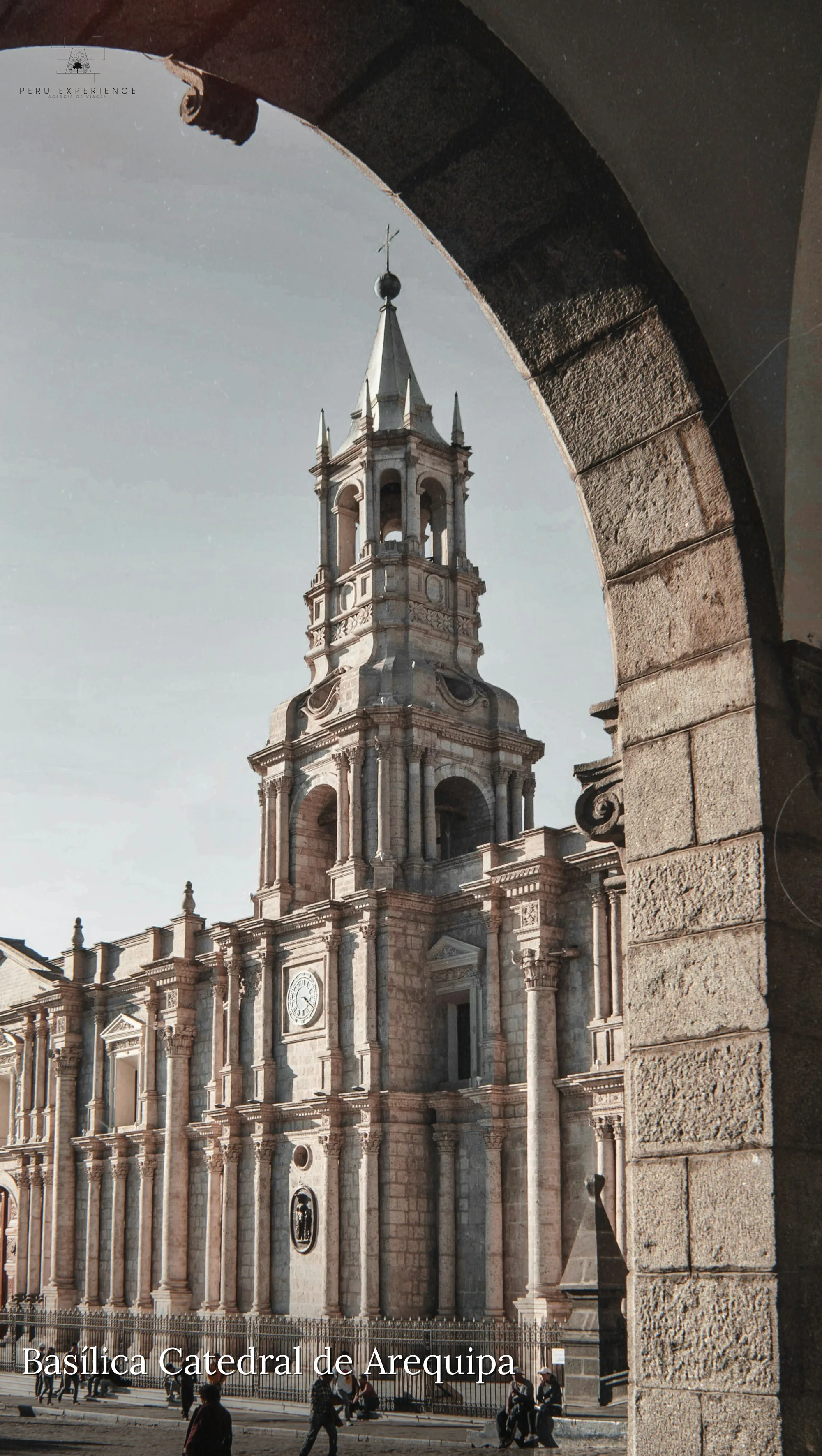 Basílica Catedral de Arequipa em pedra sillar branca emoldurada por um arco colonial dos portales da Plaza de Armas — torre neoclássica com cruz, reconstruída no século XIX após terremotos