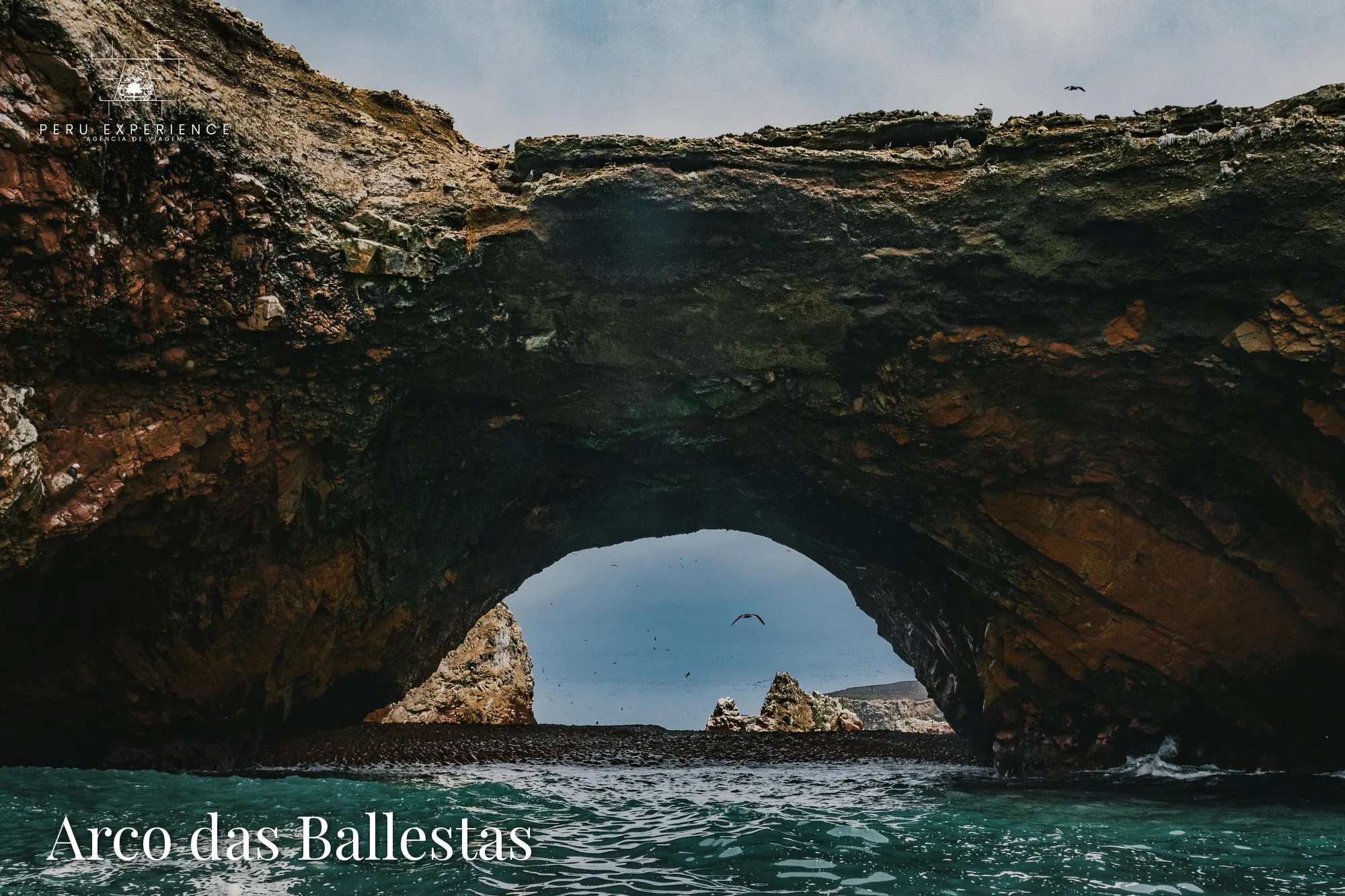 Arco rochoso natural das Ilhas Ballestas com aves marinhas em voo, formação icônica do passeio de barco em Paracas, Peru