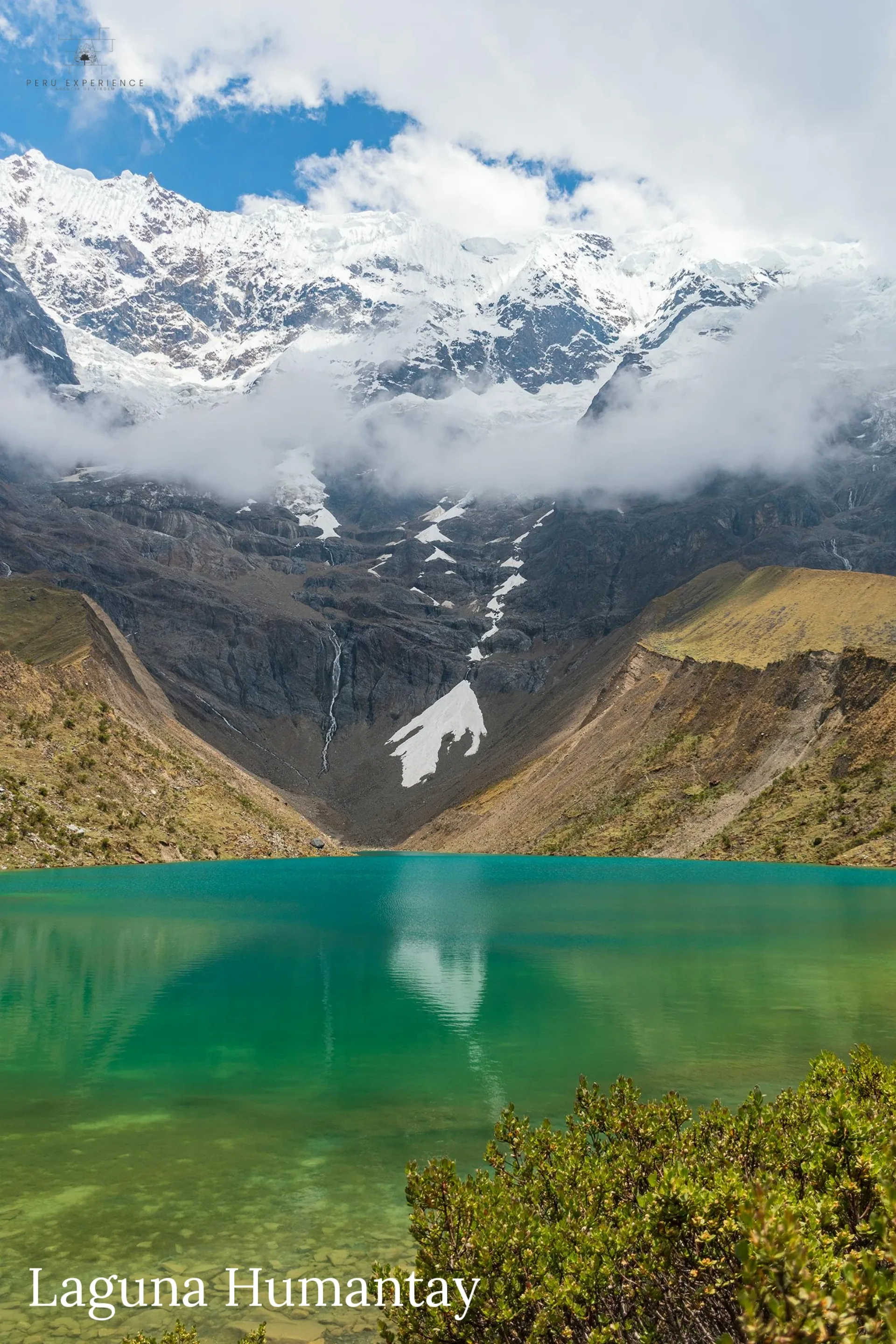 Vista panorâmica vertical da Lagoa de Humantay com suas águas turquesa-esmeralda cristalinas refletindo o imponente nevado coberto de nuvens, a 4.180 metros de altitude na Cordilheira Vilcabamba próximo a Cusco, Peru