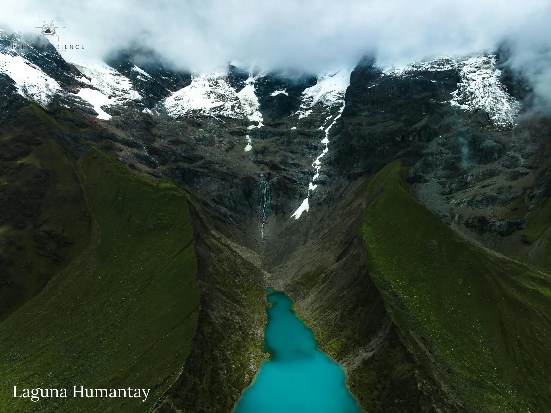 Vista aérea de drone do vale glacial da Lagoa de Humantay entre montanhas verdes e nevados — ângulo cinematográfico raro mostrando a geografia única do santuário natural a 4.180m, Cusco, Peru