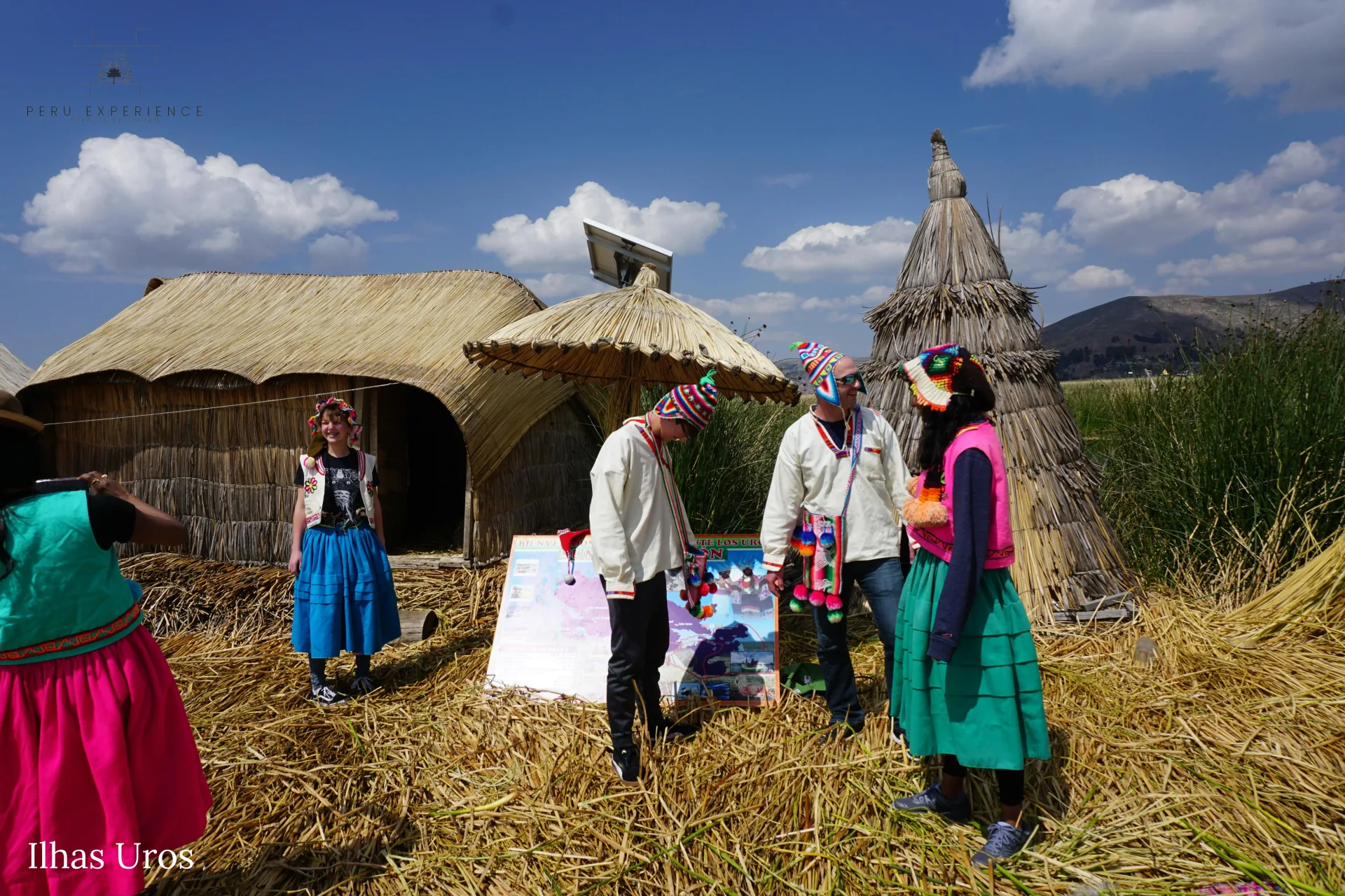 Visitantes vestindo trajes tradicionais Uros (saias coloridas, coletes bordados e gorros chullo) interagindo com a comunidade local em ilha flutuante do Lago Titicaca — experiência cultural autêntica em Puno, Peru