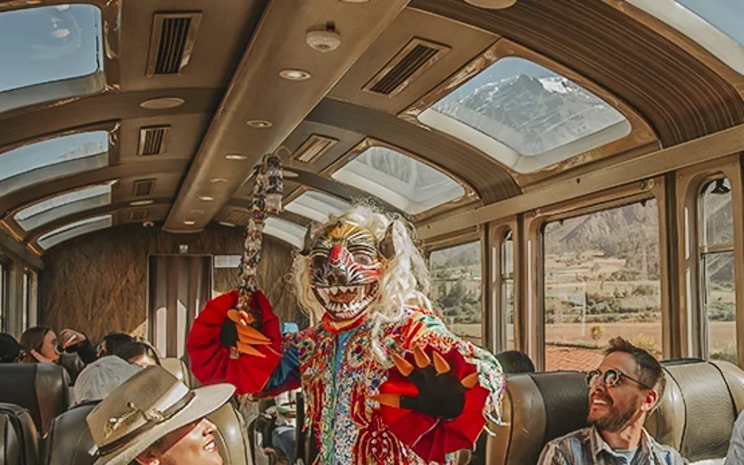 Trem para Machu Picchu: PeruRail ou Inca Rail? Guia Completo 2026 Interior panorâmico do trem Vistadome com apresentação cultural andina a caminho de Machu Picchu