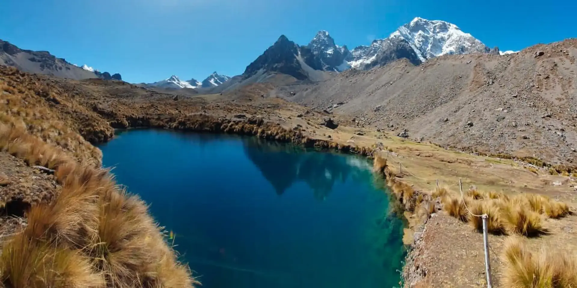 Lagoa de águas turquesa das 7 Lagunas de Ausangate rodeada por montanhas nevadas sob céu azul, Cordilheira de Vilcanota, Cusco, Peru