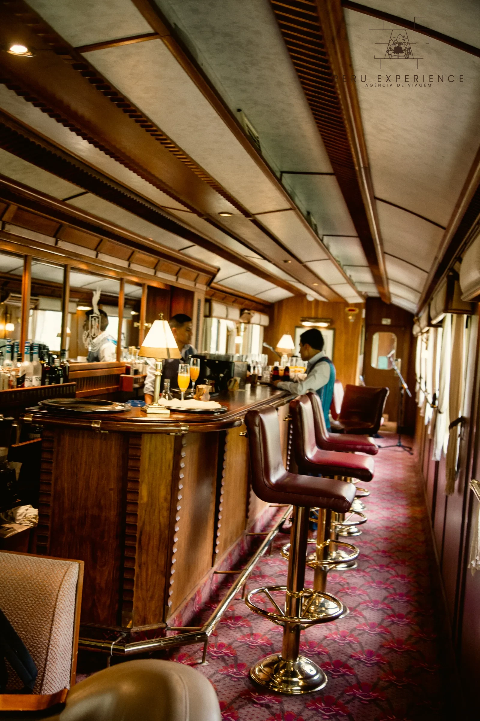 Balcão de madeira com banquetas e equipe de atendimento no trem Hiram Bingham.